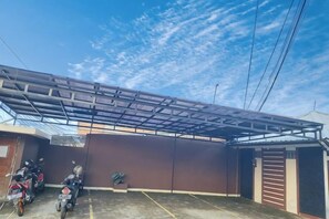 Un espace extérieur abrité, doté d’une structure de toit en métal, d’un mur brun et d’une moto garée sur le côté.