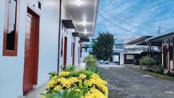 A narrow street with buildings on either side, a clear sky, and a small garden with yellow flowers.