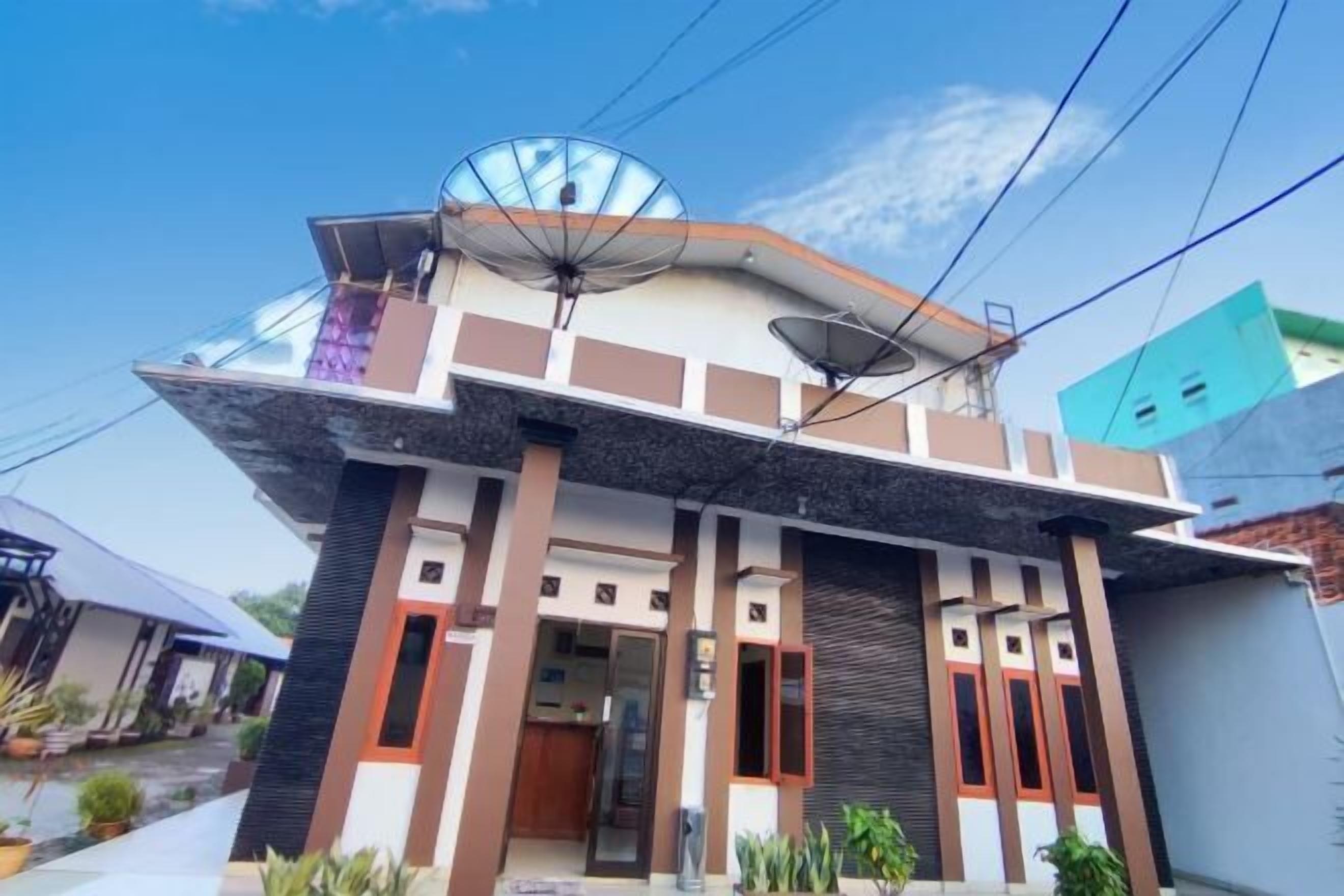 Une maison moderne à deux étages, dotée d’antennes paraboliques, d’un balcon et d’un petit jardin.