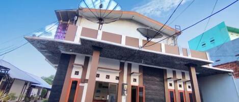 A modern two-story house with satellite dishes, a balcony, and a small garden area.