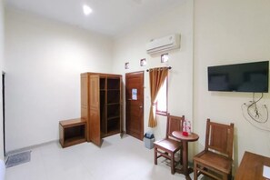 Una habitación con un armario de madera, un televisor instalado en la pared y una pequeña mesa con sillas.