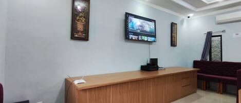 A reception area with a wooden reception desk, a flat-screen TV mounted on the wall, and a purple sofa.