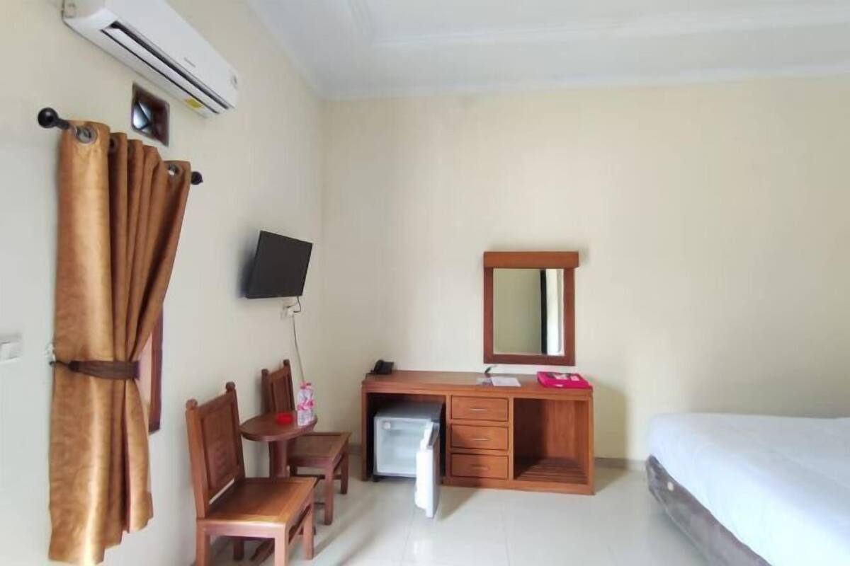A room with a bed, a desk with a mirror, a chair, a television, and an air conditioner.