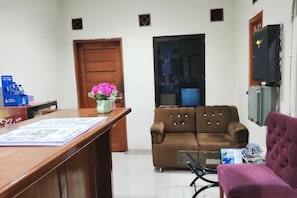 A reception area with a wooden desk, a brown sofa, a purple armchair, and a TV mounted on the wall. - HOTEL CIWANGI (Bungursari)