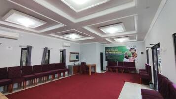 A conference room with a red carpet, multiple rows of chairs, a table, and a banner on the wall.