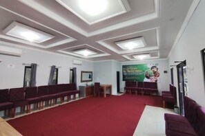 A conference room with a red carpet, multiple rows of chairs, a table, and a banner on the wall. - HOTEL CIWANGI (Bungursari)