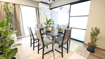 A dining area with a table set for four, surrounded by chairs, with a potted plant on the right and another on the left.