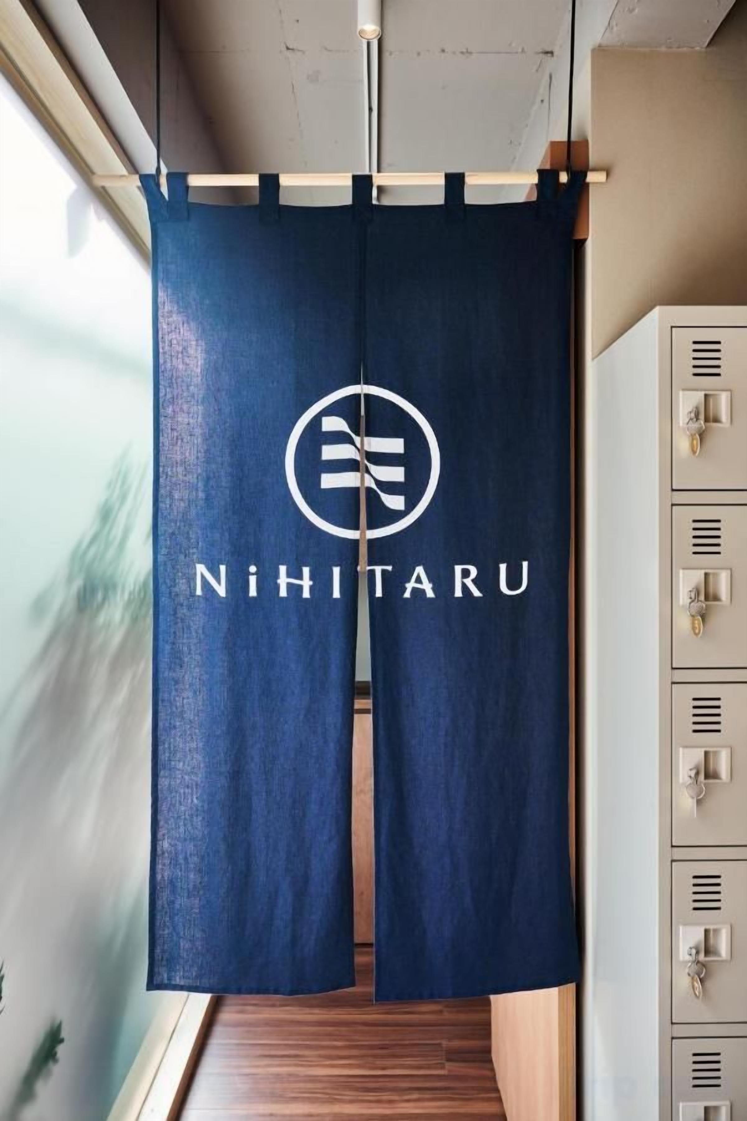 A blue curtain with a logo and the name 'NiHiTarU' hanging in a room with a wooden floor and a cabinet with keys.