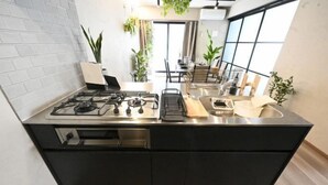 A modern kitchen with a gas stove, black cabinets, and a large window. - NiHITARU Stay (Tokyo)