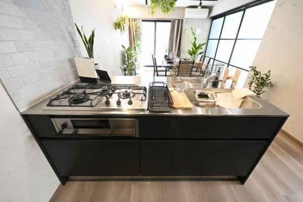 A modern kitchen with a gas stove, black cabinets, and a large window. - NiHITARU Stay (Tokyo)