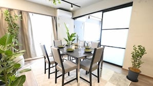 A dining area with a table set for four, surrounded by chairs, with large windows and potted plants. - NiHITARU Stay (Tokyo)