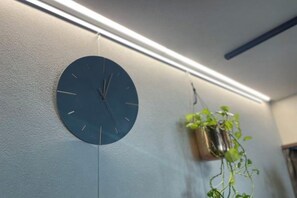 Ένα ρολόι τοποθετημένο στον τοίχο και ένα φυτό σε κρεμαστή γλάστρα σε ένα δωμάτιο.
