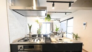 A modern kitchen with a gas stove, stainless steel appliances, and black cabinetry. - NiHITARU Stay (Tokyo)