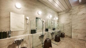 A modern bathroom with a glass shower enclosure, a large mirror, and a vanity with toiletries. - NiHITARU Stay (Tokyo)