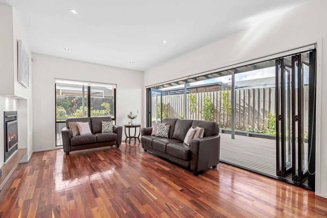 A spacious living room with hardwood flooring, two dark sofas, a small round table, and a fireplace.