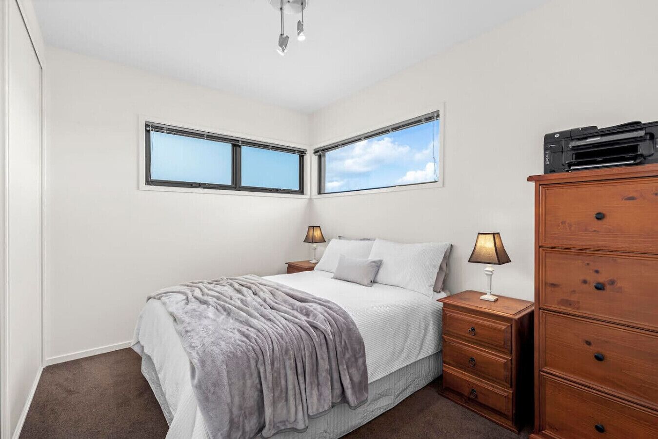 A bedroom with a bed, two bedside tables, a dresser, and two windows.