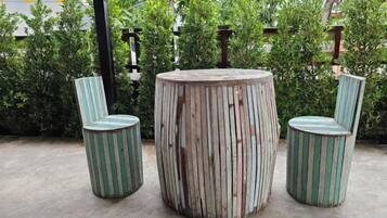 A round wooden table with two striped chairs, set outdoors with greenery in the background.