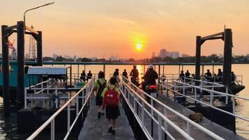 A pier with people walking and sitting, a sunset in the background, and a city skyline.