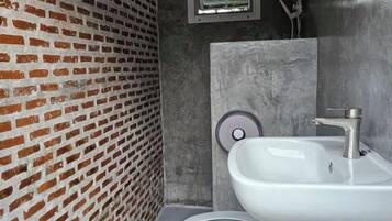 A bathroom with a white sink, a toilet, and a brick wall.
