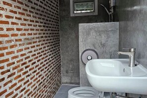 Un baño con un lavamanos blanco, un inodoro y una pared de ladrillo.