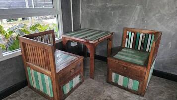 A small wooden table and two chairs with green and white striped cushions, positioned near a window with a view of greenery.