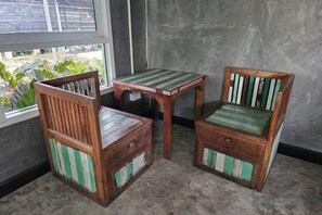 A small wooden table and two chairs with green and white striped cushions, positioned near a window with a view of greenery. - The Bird Nest Homestay& Coffee Shop (Phra Pradaeng)