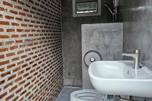 A bathroom with a brick wall, a white sink, and a toilet. - The Bird Nest Homestay& Coffee Shop (Phra Pradaeng)