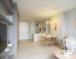 Una sala moderna con televisor, comedor con mesa y sillas, sofá y cocina al fondo.