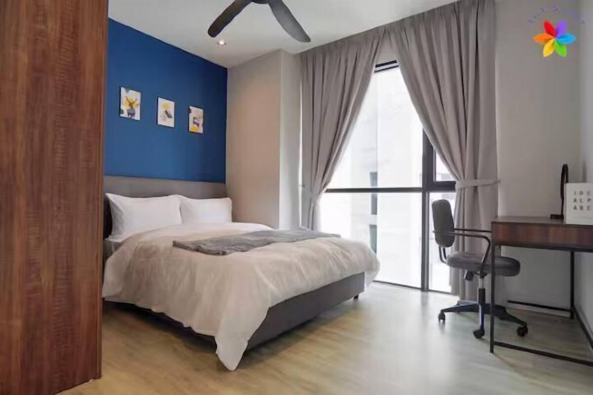 A bedroom with a bed, a desk, and a window with curtains.