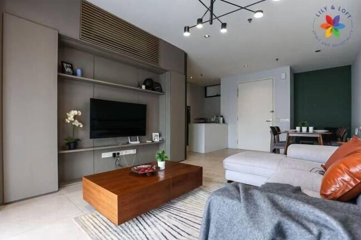 A modern living room with a flat-screen TV, a wooden coffee table, a sofa, and a dining area with a table and chairs.