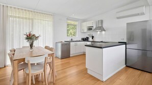 A modern kitchen with white cabinetry, a central island, and a stainless steel refrigerator. - Prasino in Central Lorne (Lorne)