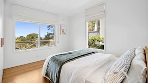 A bedroom with a bed, two windows, a view of the outdoors, and a wooden floor. - Prasino in Central Lorne (Lorne)