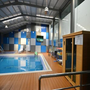 Uma área de piscina com deck de madeira, cadeiras de descanso e uma tela de televisão na parede.