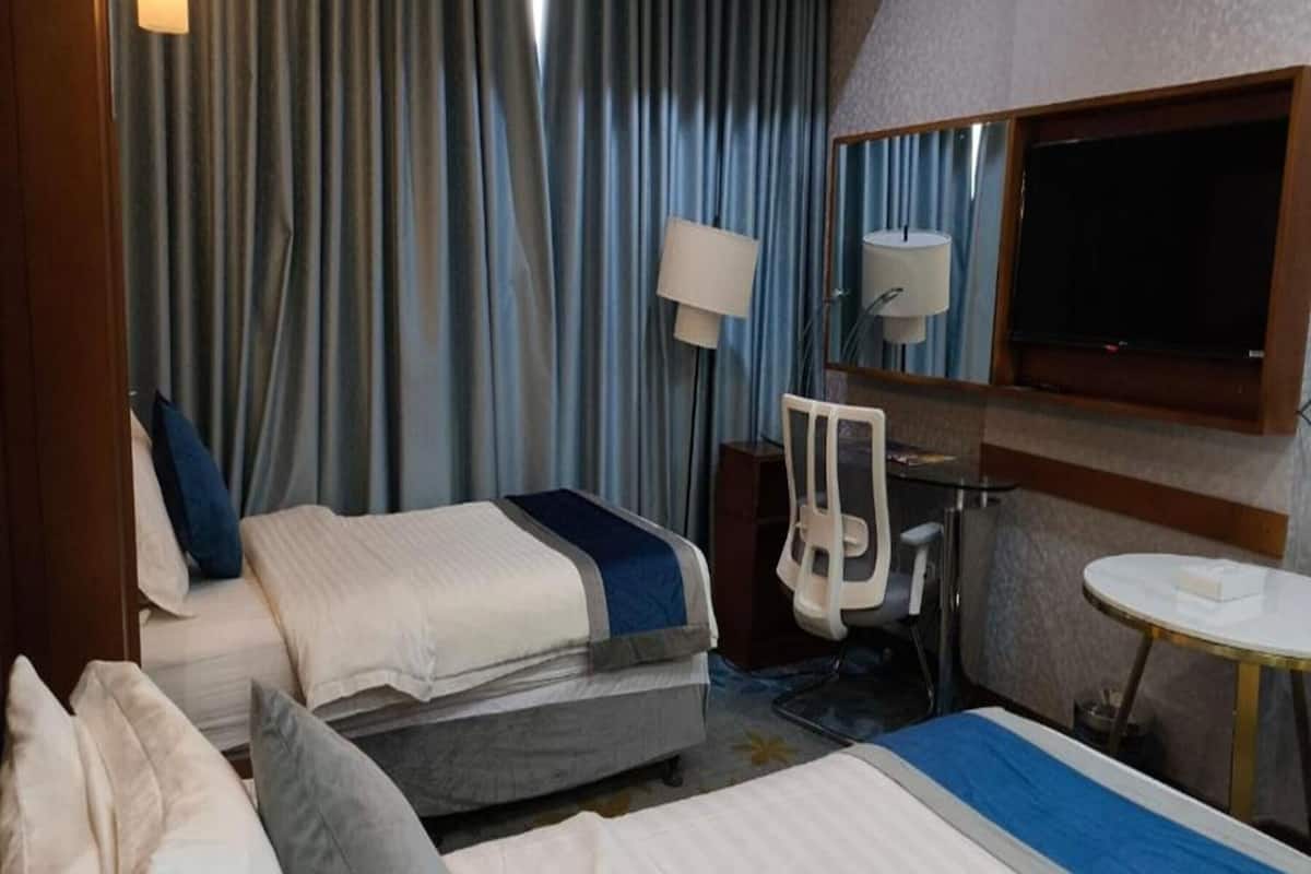 Une chambre d’hôtel avec deux lits, un bureau, une chaise, une télévision et une fenêtre avec des rideaux.