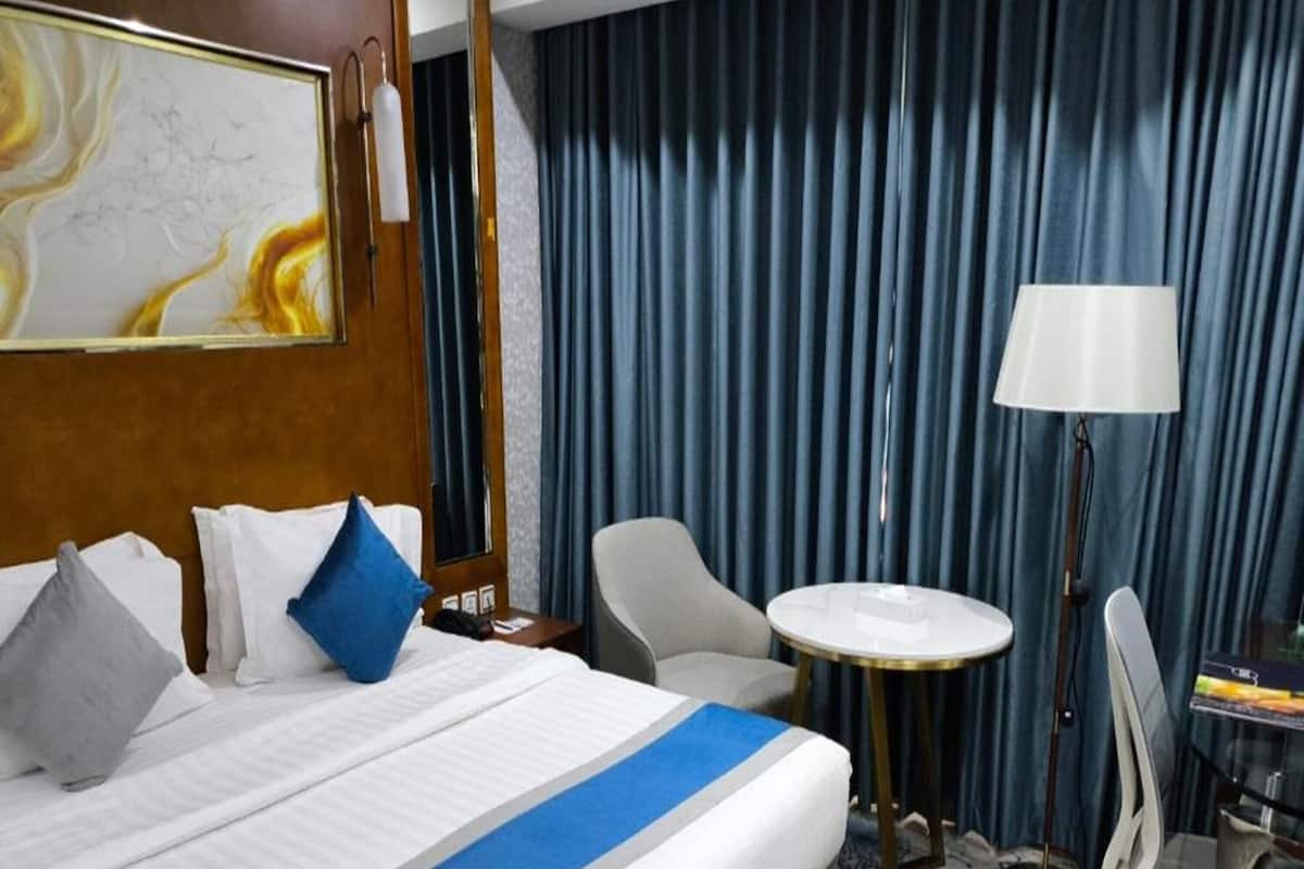 Une chambre d’hôtel avec un grand lit, une table ronde, une chaise, un bureau et une lampe.