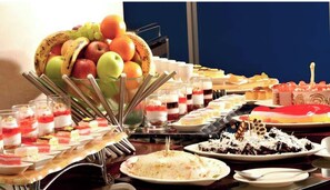 Buffet com diversos doces, frutas e bebidas.