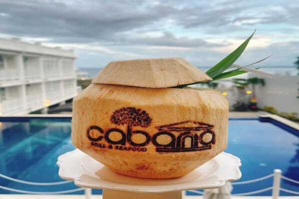 Un coco con un logo y texto, sobre un pedestal blanco cerca de una piscina.