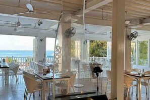 An indoor dining area with tables and chairs, large windows, and a view of the sea. - The Mark Resort Cebu (Lapu-Lapu City)