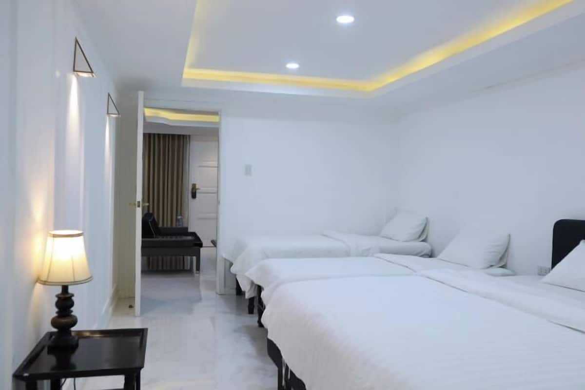 A hotel room with two beds, a nightstand, a lamp, and a view of a hallway.