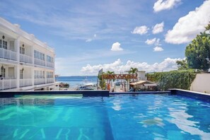 En swimmingpool med utsikt över havet, en byggnad med balkonger och en klar himmel.