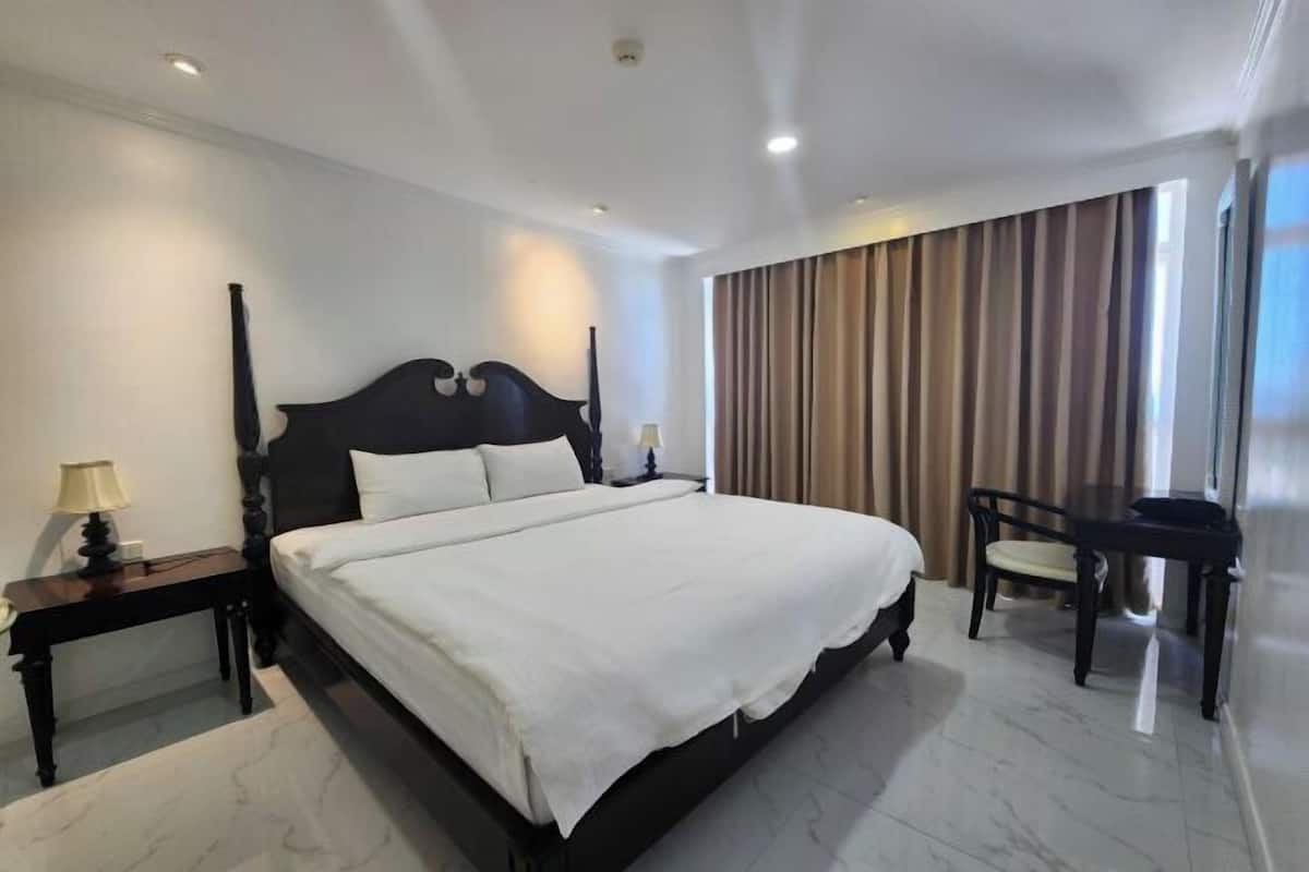 A hotel room with a large bed, a desk, a chair, a lamp, and a window with curtains.