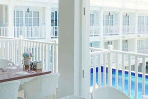 A balcony with white wicker furniture, a dining table, and a view of a pool and upper levels of a building. - The Mark Resort Cebu (Lapu-Lapu City)