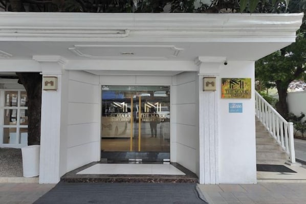 L’entrée d’un hôtel, avec une façade blanche, une porte en verre et un escalier menant à l’étage supérieur.