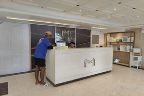 A reception desk with a logo, a man standing beside it, and a counter with items on it. - The Mark Resort Cebu (Lapu-Lapu City)
