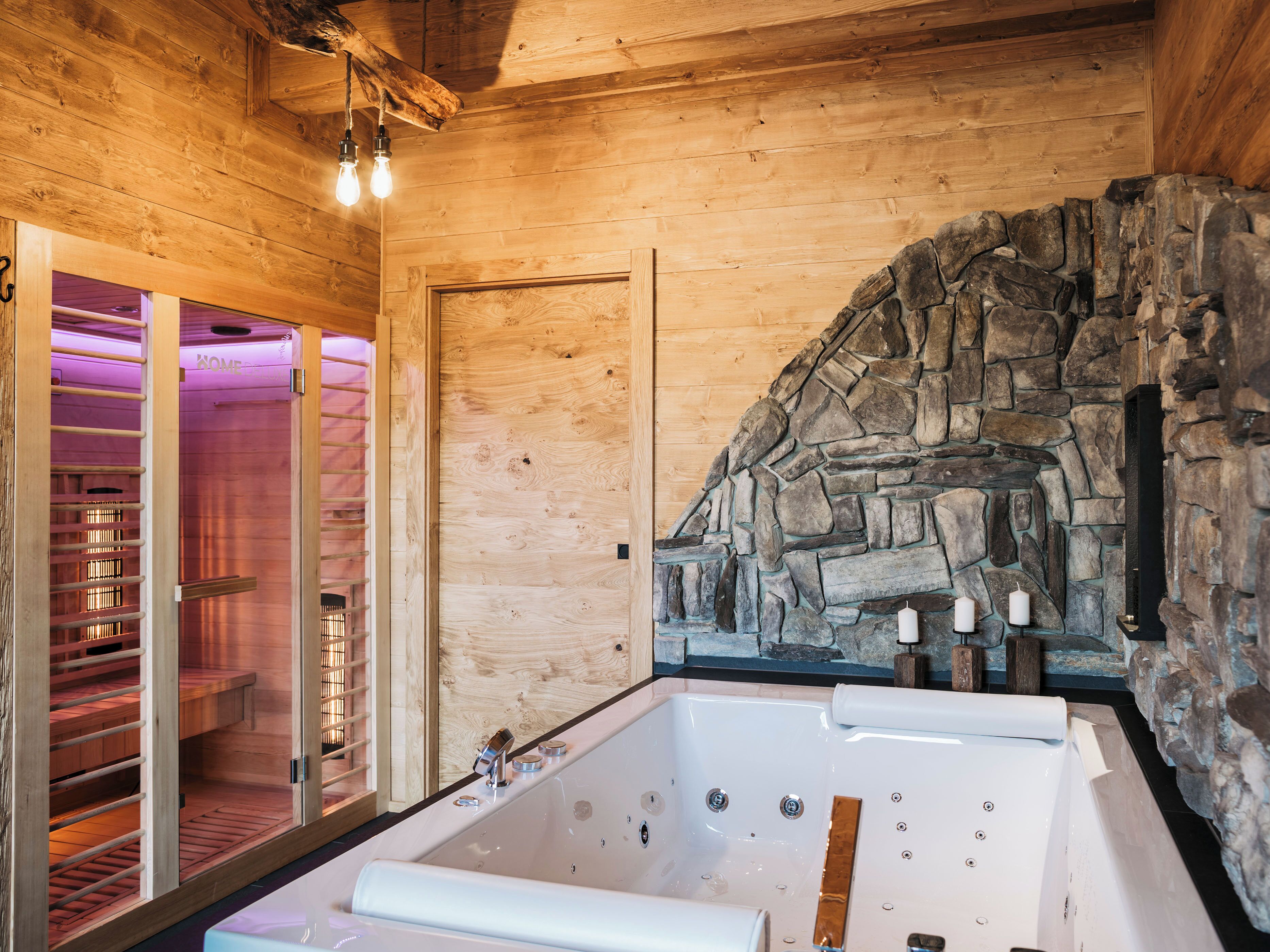 Un intérieur en bois avec un mur en pierre, une porte en verre donnant accès à un espace sauna et une grande baignoire.