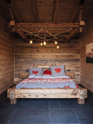 A wooden cabin-style bedroom with a bed, checkered pillows, a red heart pillow, and string lights.