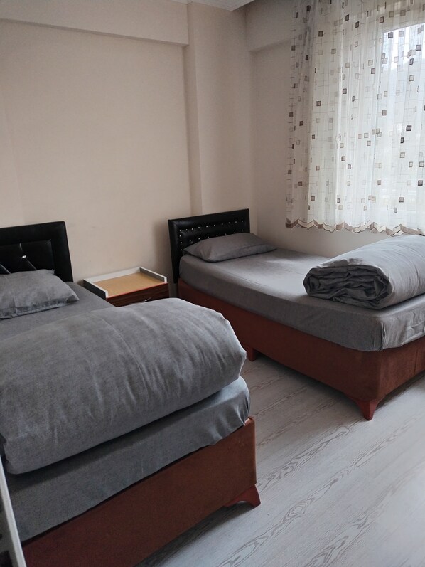 A room with two beds, a wooden nightstand, and a window with patterned curtains.