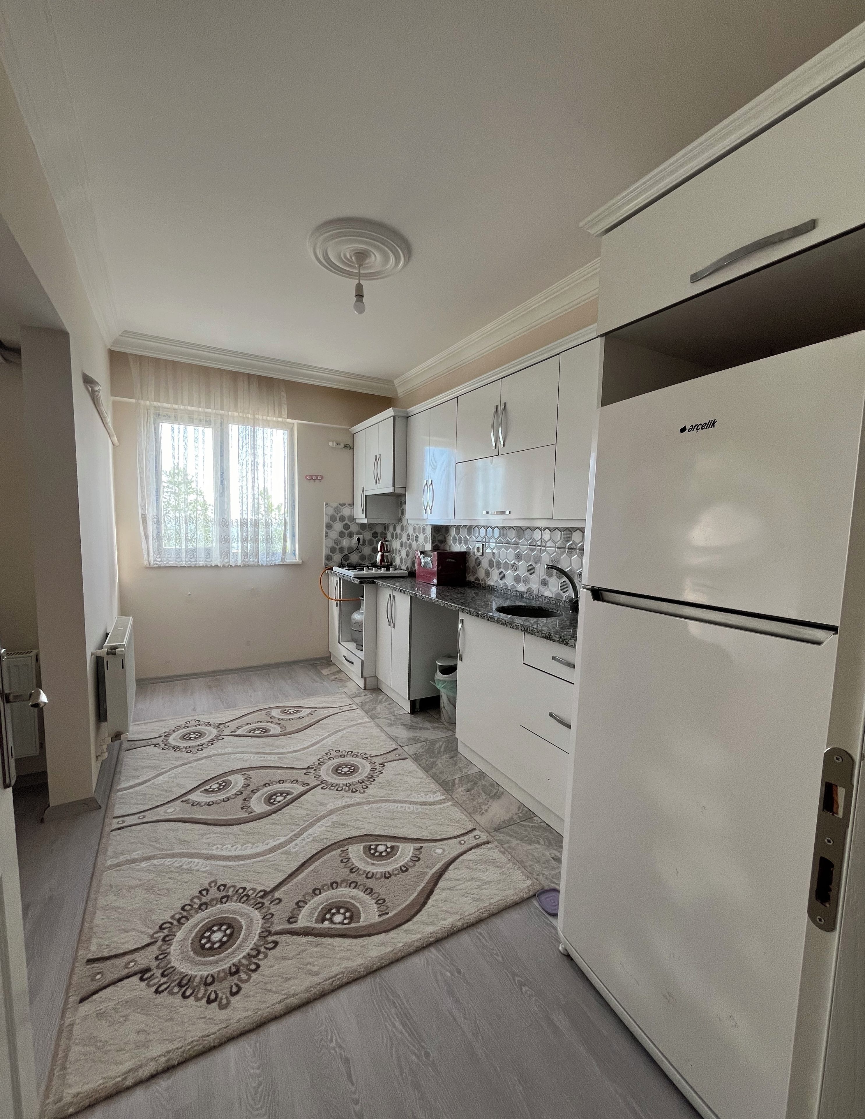 A kitchen with white cabinets, a refrigerator, and a patterned rug.