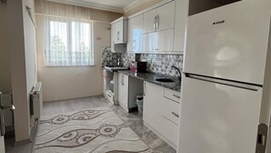 A kitchen with white cabinets, a refrigerator, and a patterned rug. - ÜNYE KAVAKLAR GÜNLÜK EV (Ünye)