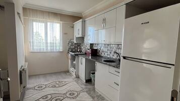 A kitchen with white cabinets, a refrigerator, and a patterned rug.